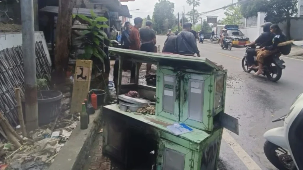 Rombong bakso yang hangus terbakar bersama sepeda motor terlihat terparkir di pinggir Jalan Raya Akah, Klungkung, usai insiden kebakaran pada Rabu (23/7/2025) siang. Warga tampak masih berkumpul di lokasi kejadian. (Foto: Istimewa)