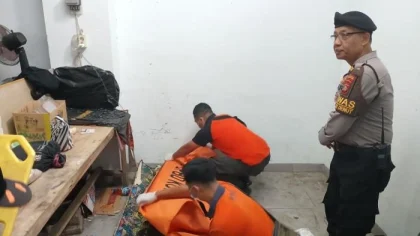 Petugas mengevakuasi jenazah pria yang ditemukan meninggal dunia di sebuah ruangan sempit di Denpasar, Bali, dengan pengawasan anggota kepolisian. (Foto: Istimewa)