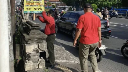 Petugas Satpol PP Kota Denpasar menurunkan salah satu alat peraga promosi yang dipasang sembarangan di fasilitas umum saat penertiban di wilayah Jalan Raya Sesetan, Rabu (2/7/2025). (Foto: Istimewa)